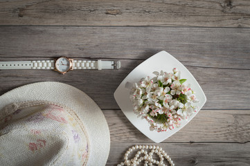 Cup of blooming flowers pear tree, beads from pearls, white clock, wicker hat on a gray background. 