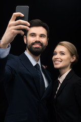 smiling business people taking selfie on smartphone isolated on black