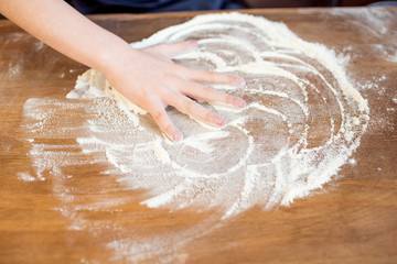 little child making pizza dough on wooden tabletop in kitchen