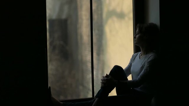 Silhouette of woman sitting on the sill and looking out the window