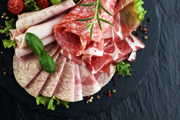 Food tray with delicious salami, pieces of sliced ham, sausage, tomatoes, salad and vegetable -...