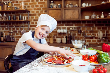 side view of little smiling boy making pizza