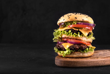 Big juicy hamburger with vegetables and beef on black background. Vintage toned - obrazy, fototapety, plakaty