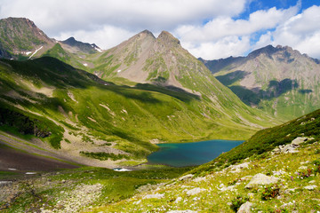 Fototapeta na wymiar Mountain Lake in the mountains of Western Caucasus. Bright blue sky and white clouds.
