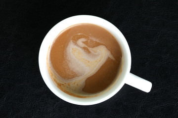 Coffee ready mix in the cup represent cream layer floating on the coffee surface put on black color leather platemat.