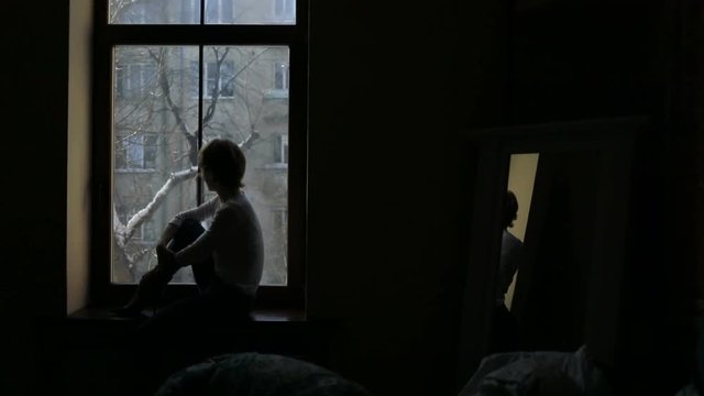 Silhouette of a woman sitting on the sill and looking out the window