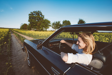 Young female driver driving a big V8 American muscle car on open road. Road trip, journey with classic car.