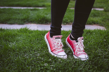 Fototapeta na wymiar Female shoes on green grass. She is wearing black pants and pink sneakers.