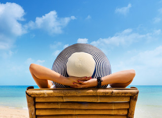 Woman in hat relaxing on beach, looking at sea.