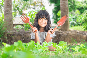Young girl holding gardening shovel and fork  in vegetable bed - 145932193