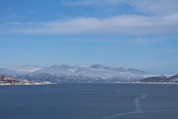 view from boat on Tromso landscape with snowy mountains and city harbor in sunny blue sky, Norway