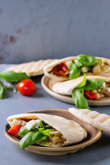 Pita bread sandwiches with grilled vegetables paprika, eggplant, tomato, basil and feta cheese served on terracotta plate over gray stone background. Healthy fast food concept.