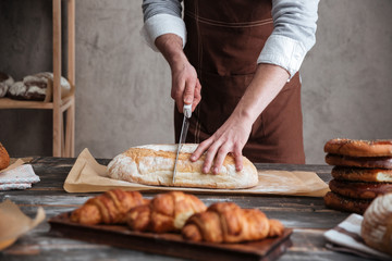 Cropped image of young man baker cut the bread.