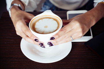 Close up hands of woman holding cup of hot cappuccino coffee in the cafe