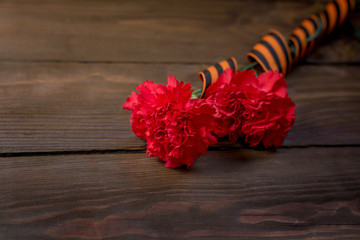 Red carnations and St. George ribbon on wooden background/St. George ribbon - the symbol of the great Victory/Victory Day