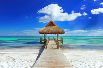 Tropical white sandy beach. Palm leaf roofed wooden pier with gazebo on the beach. Cross processed. Instagram filter. Punta Cana, Dominican Republic