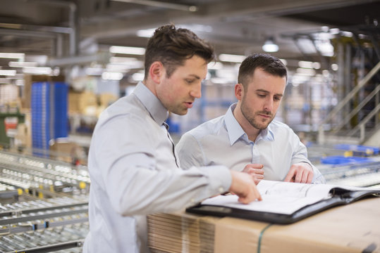 Two men in factory warehouse looking at documents