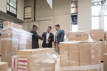 Three men in factory warehouse surrounded by cardboard boxes