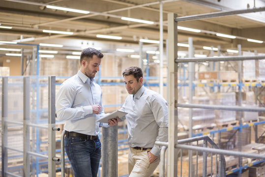 Two men in factory warehouse looking at tablet
