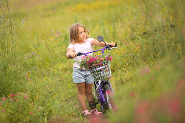 Little cute girl riding a bike with basket full of flowers. Cheerful child