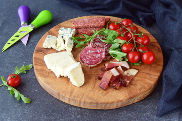 Olive wood cutting board with cherry tomatoes, arugula and variety of sliced cheeses and sausages. Snack concept