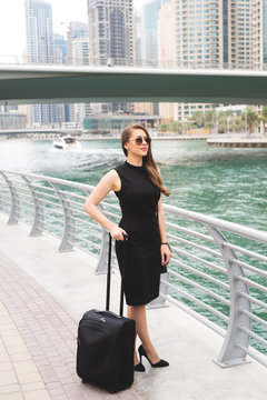 Attractive young business woman pulling suit case trough the magnificent city. Beautiful city scape panoramic view.