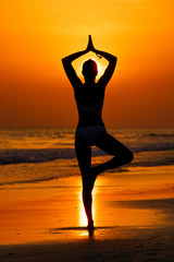 Fototapeta Kobieta ćwicząca jogę na plaży przy zachodzie słońca obraz