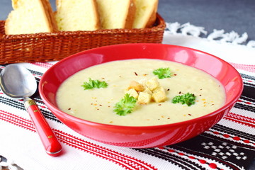 Cream of Vegetable with Cauliflower and cream in a red ceramic bowl on a textile background. Healthy eating concept