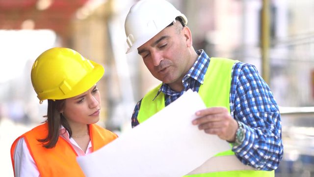 Male and female construction engineers holding plans and inspecting the construction site among scaffolding