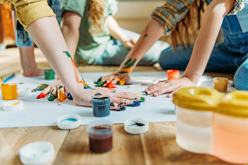 cute kids painting on paper with hands while sitting on floor