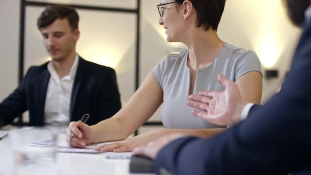 Tilt down of smiling woman and two businessmen discussing something at meeting. Slow motion footage