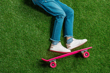 Top view of cute little girl with pink skateboard lying on green lawn