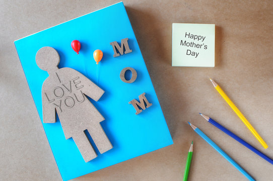 Wooden of women, mom word with balloon, colored pencil and sticky note on brown background, happy mothers day concept and holiday and event idea