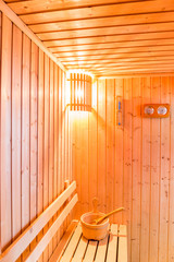 Sauna accessories in sauna room, wooden bucket place on bench and bath thermometer and timer on wooden wall.