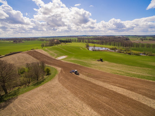 Aerial view of beautiful agricultural fields in spring with a tractor at work - tractor plough cultivating fields