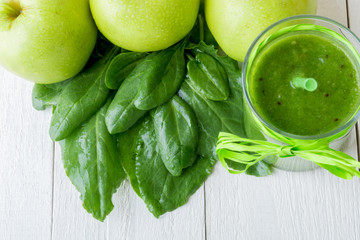 Green smoothie near ingredients for it on white wooden background. Apple, lime, spinach. Detox. Healthy drink.