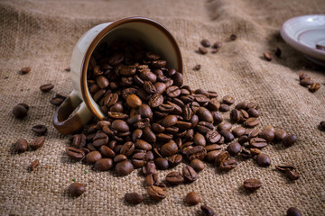 White Cup full of roasted coffee beans on rustic old cloth