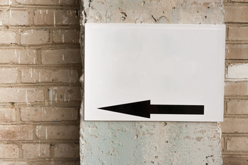 White sheet metal with black arrow nailed to concrete column on old grey brick wall.