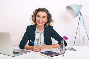 Woman is sitting at her desk with a laptop and tablet.Woman at the office,woman in black jacket,curly hair,working space,white background,busy,office manager,best worker,businesswoman,new idea,happy