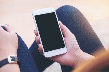 Mockup image of a woman sitting on the street and holding mobile phone with blank black screen