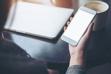 Mockup image of mobile phone with blank white screen with latop and coffee cup on wooden table in cafe