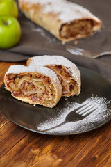 Apple strudel with icing sugar on black plate, wooden background