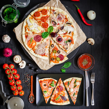 Pizza with ingredients, spices, oil and vegetables on dark background. Flat lay, top view. Tasty italian food