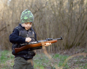 Cute  child in soldier uniform playing toy gun outdoors