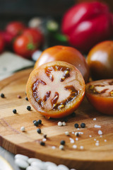 Halves of Kumato tomatoes on wooden board surrounded by vegetables and spices.