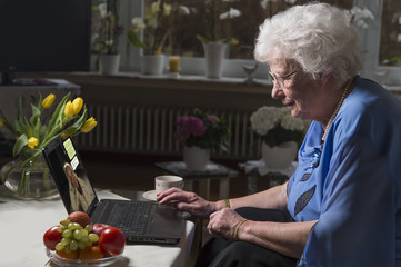 Seniorin sitzt im Wohnzimmer und schreibt Nachrichten am Laptop