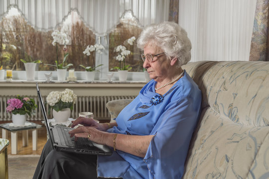 Seniorin sitzt auf Couch schreibt etwas auf dem Laptop eigene Wohnung