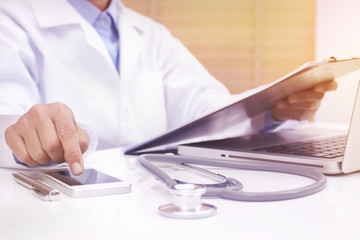 Woman doctor using mobile smart phone and reading diary at office desk