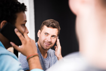 Obraz premium Smiling man looking at colleague talking on smartphone at small office meeting