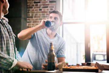 Group of happy young people having fun with beer and pizza at home